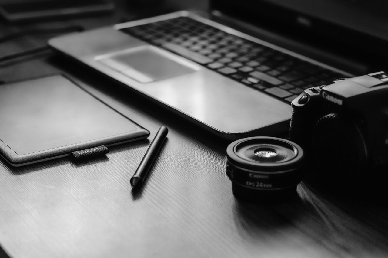 Services A monochromatic workspace with a camera, laptop, lens, and tablet, ideal for photographers.